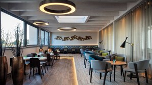 A modern dining area with round tables, chairs, and a decorative wall. - Holiday Inn Villingen - Schwenningen by IHG (Villingen-Schwenningen)