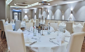 A hotel dining area with round tables set for a meal, each with cutlery, glasses, and a bottle of water.