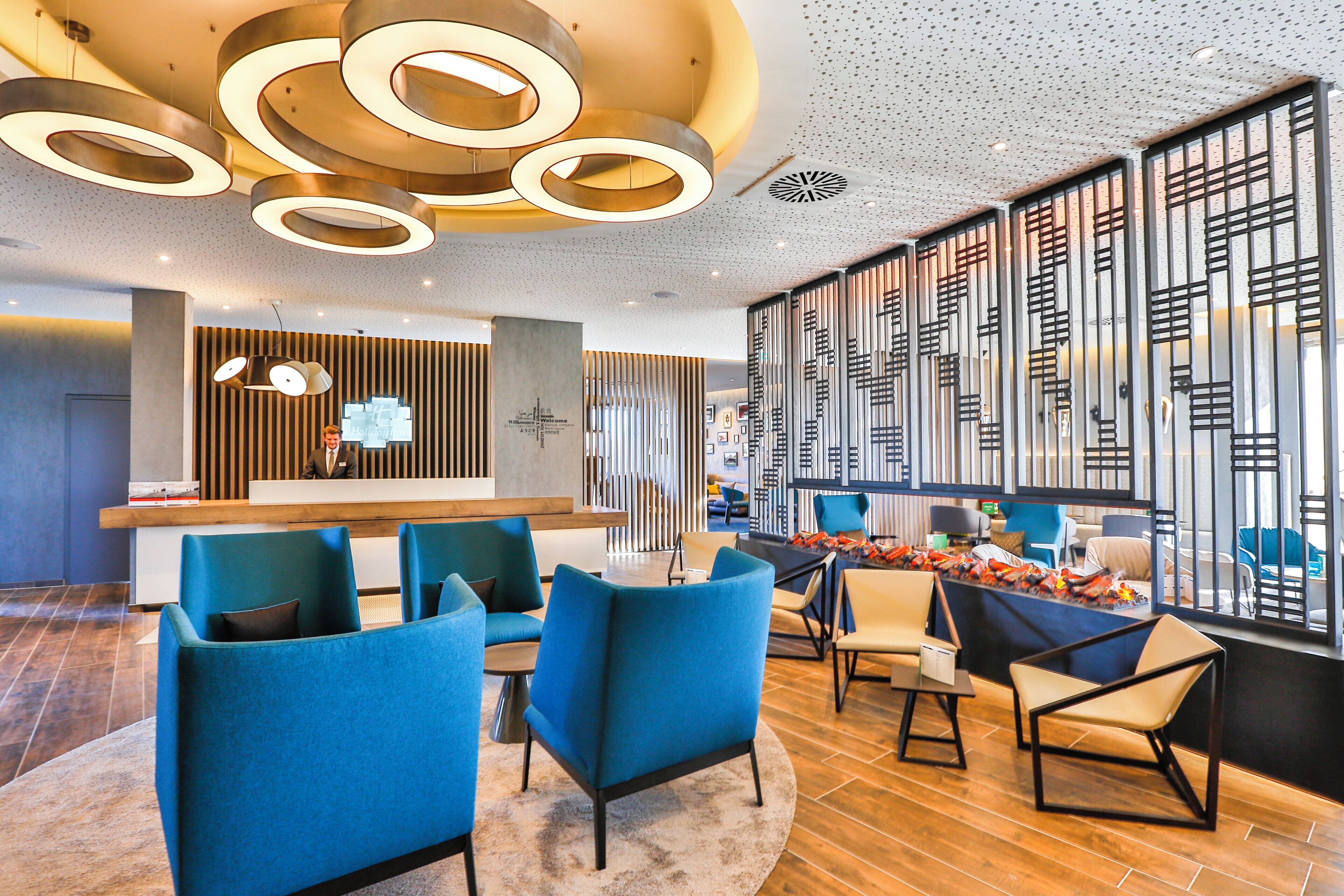 Een moderne hotellobby met een receptiebalie, blauwe zitplaatsen en decoratieve wandpanelen.