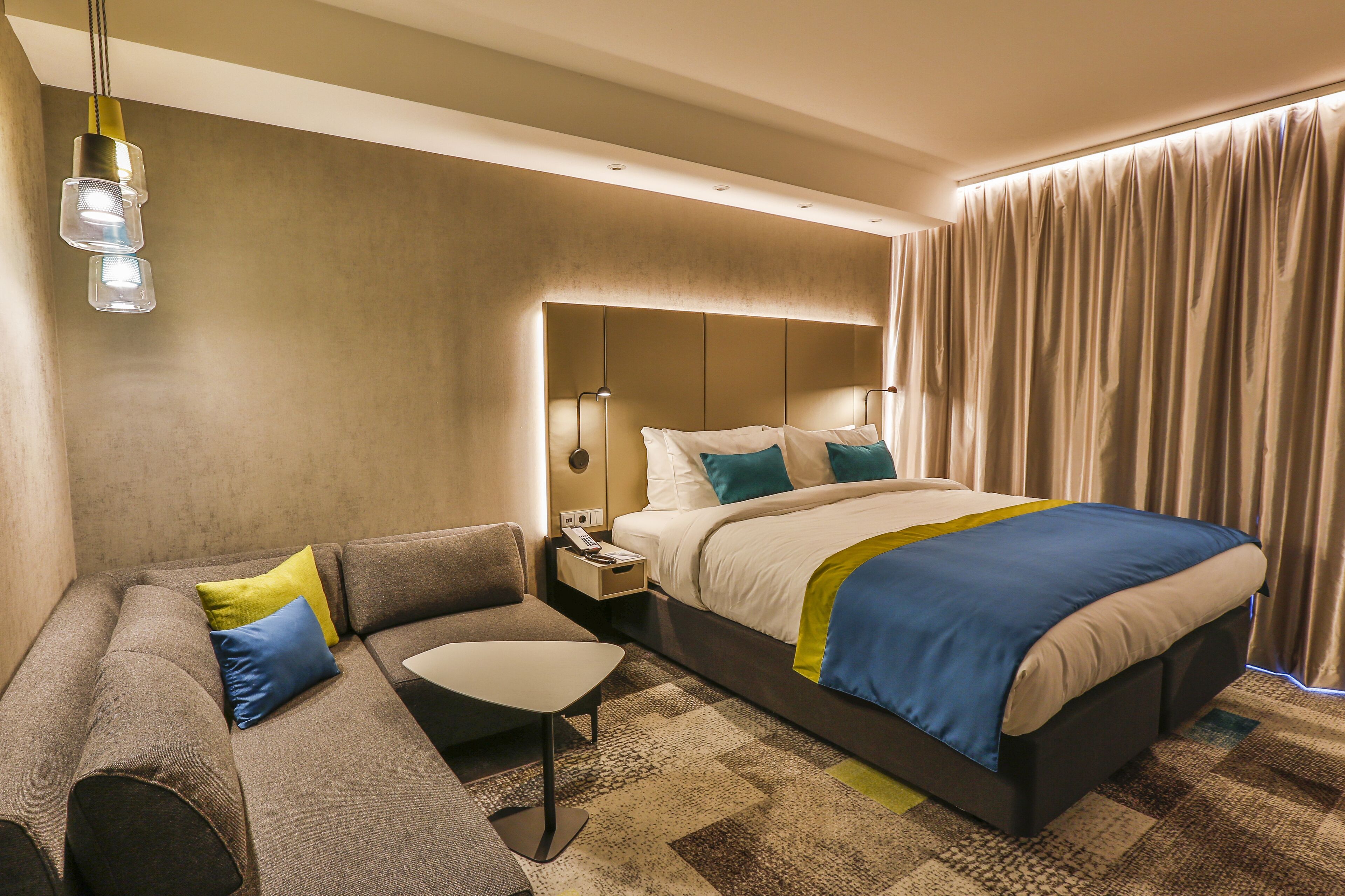 A modern hotel room with a large bed, a sofa, a small table, and a nightstand.