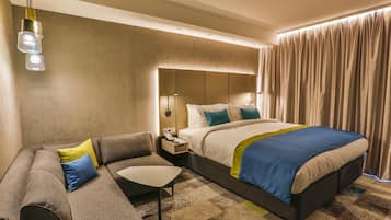 A modern hotel room with a large bed, a sofa, a small table, and a nightstand.