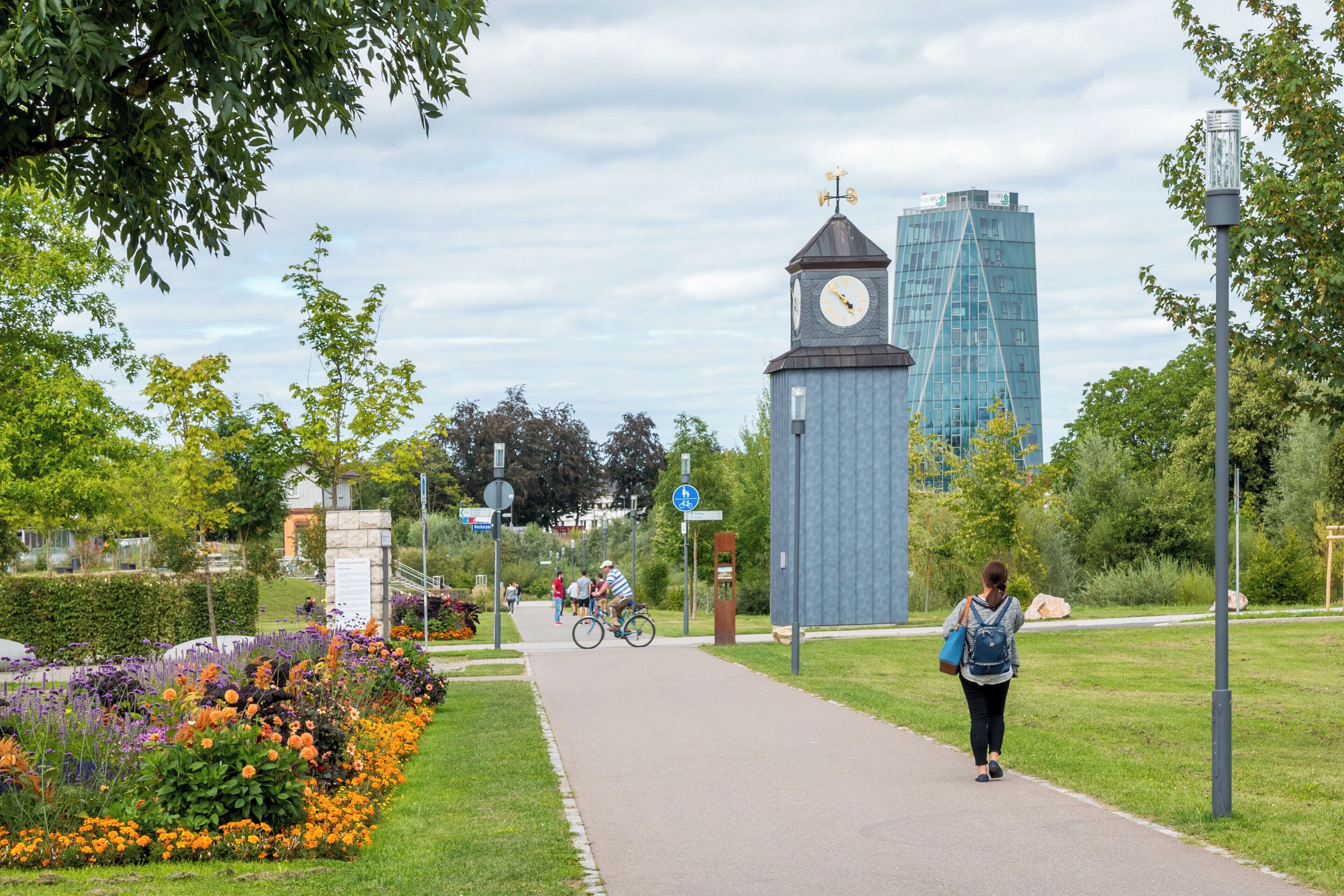A pathway with a clock tower and modern buildings in the background.