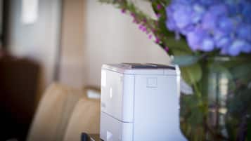 A printer on a desk with a vase of flowers in the background.