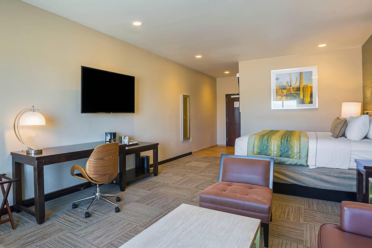 A hotel room with a bed, a desk with a chair, a television, and a painting on the wall.