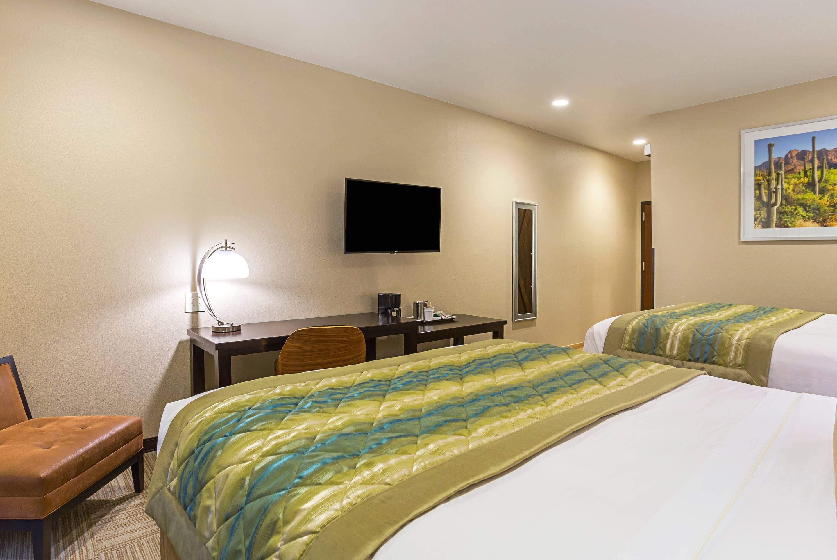 A hotel room with two beds, a desk, a chair, a TV, and a painting on the wall.