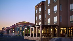 A hotel with a modern design, featuring a prominent sun emblem on the facade, a covered outdoor area with stone pillars, and a large dome structure in the background. - The Hotel at Sunland Park Casino El Paso, an Ascend Collection Hotel (Sunland Park)