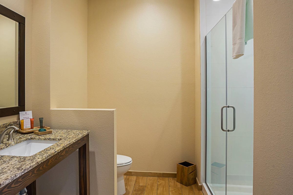 A bathroom with a granite countertop sink, a toilet, and a glass shower enclosure.