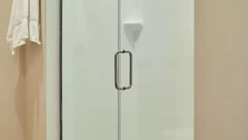 Una ducha con cerramiento de vidrio, un agarrador metálico, una toalla blanca colgada en la pared y un piso de madera.
