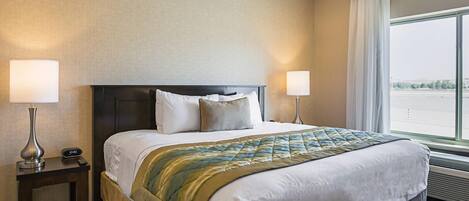 Habitación de hotel con una cama grande, dos mesitas de noche con lámparas, vista al exterior por un ventanal amplio y un diseño moderno.
