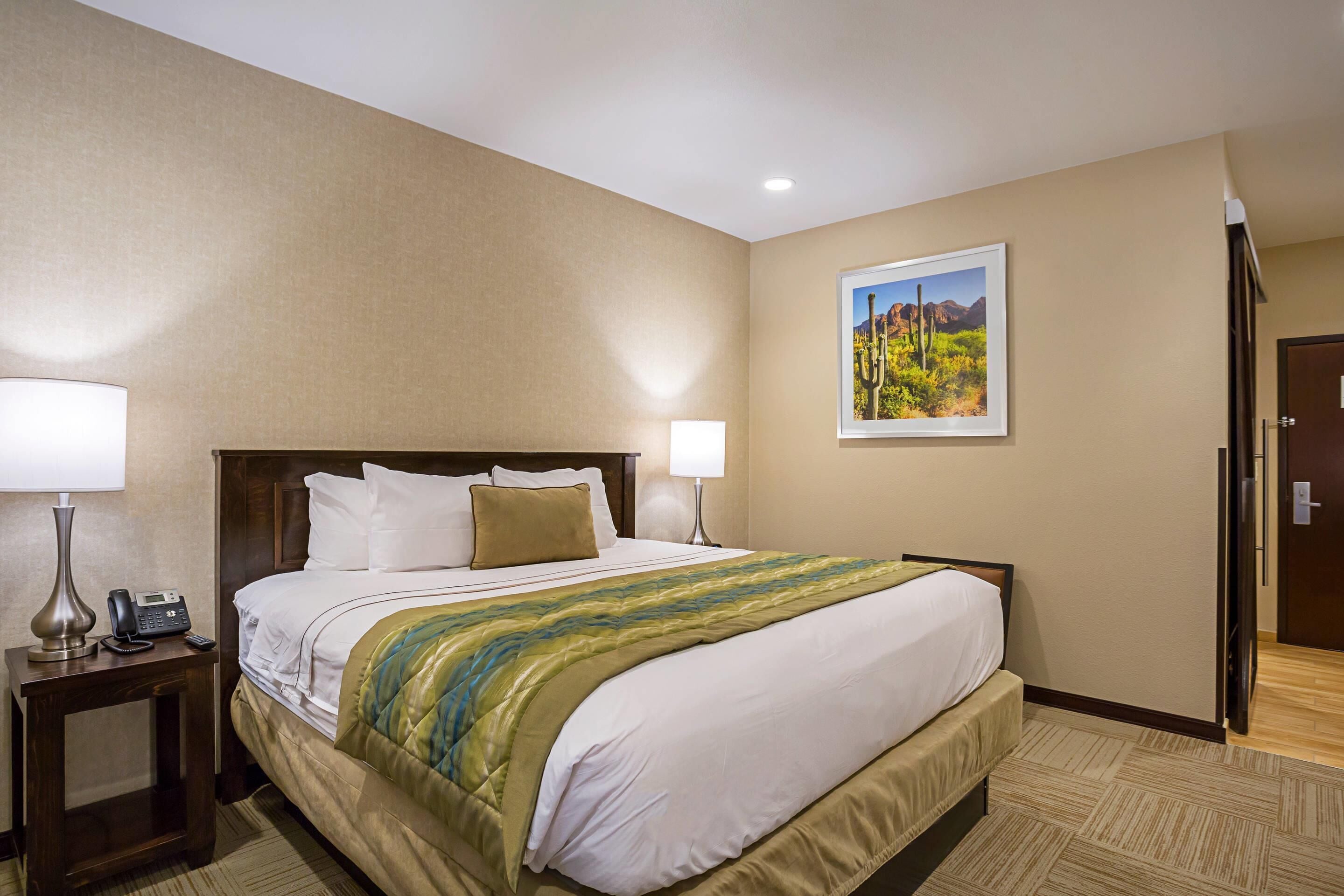 A hotel room with a large bed, two bedside tables with lamps, a painting on the wall, and a door to the right.