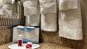 A bathroom with a mirror, white towels, a soap dispenser, and a lotion bottle on the counter.