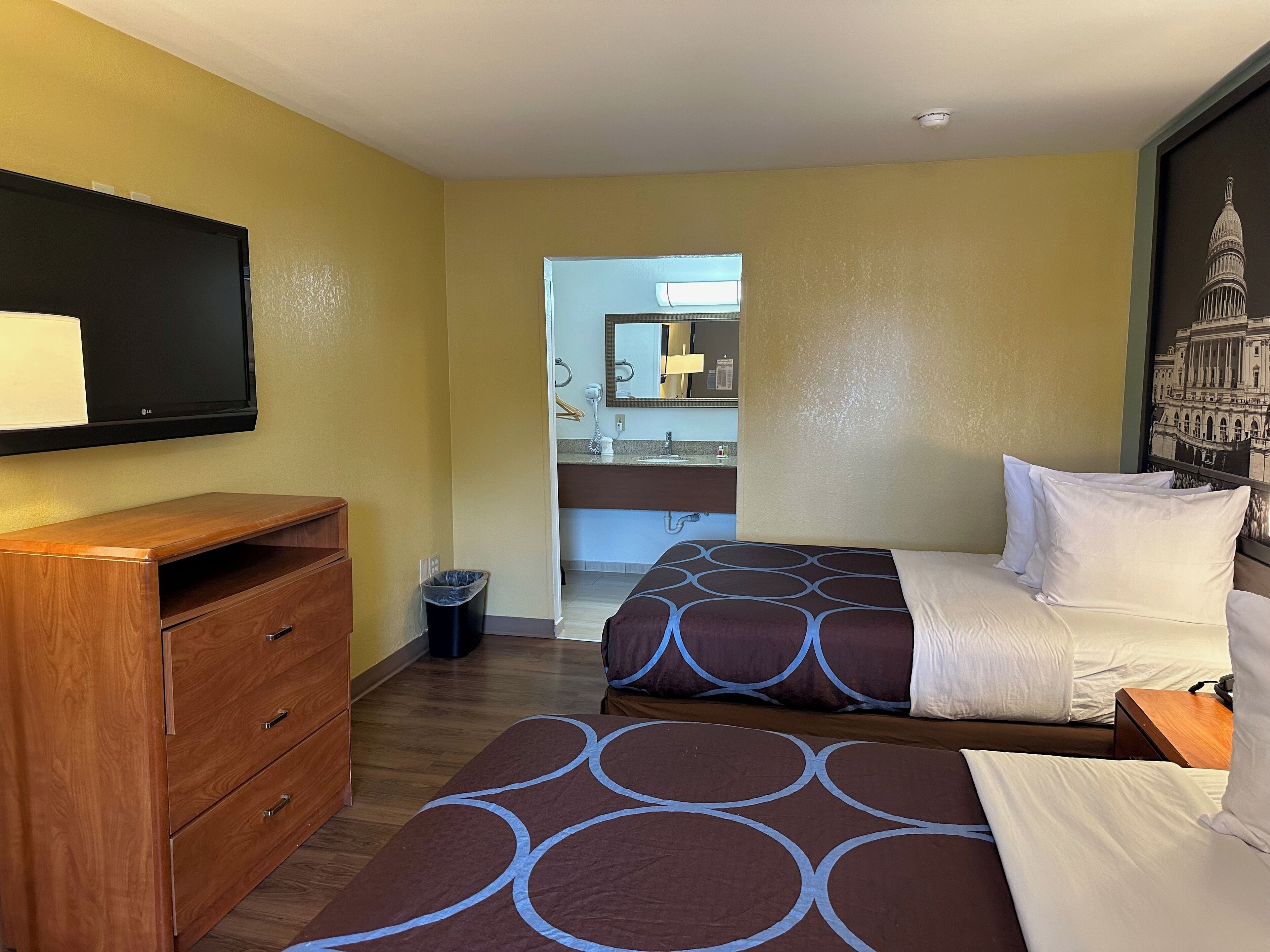 Habitación de hotel con dos camas, un aparador de madera, televisor y un baño visible a través de una puerta abierta.