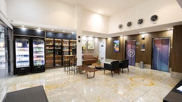 Un hall de hotel con mostrador de recepción, zona de estar, máquinas expendedoras y un panel informativo digital.
