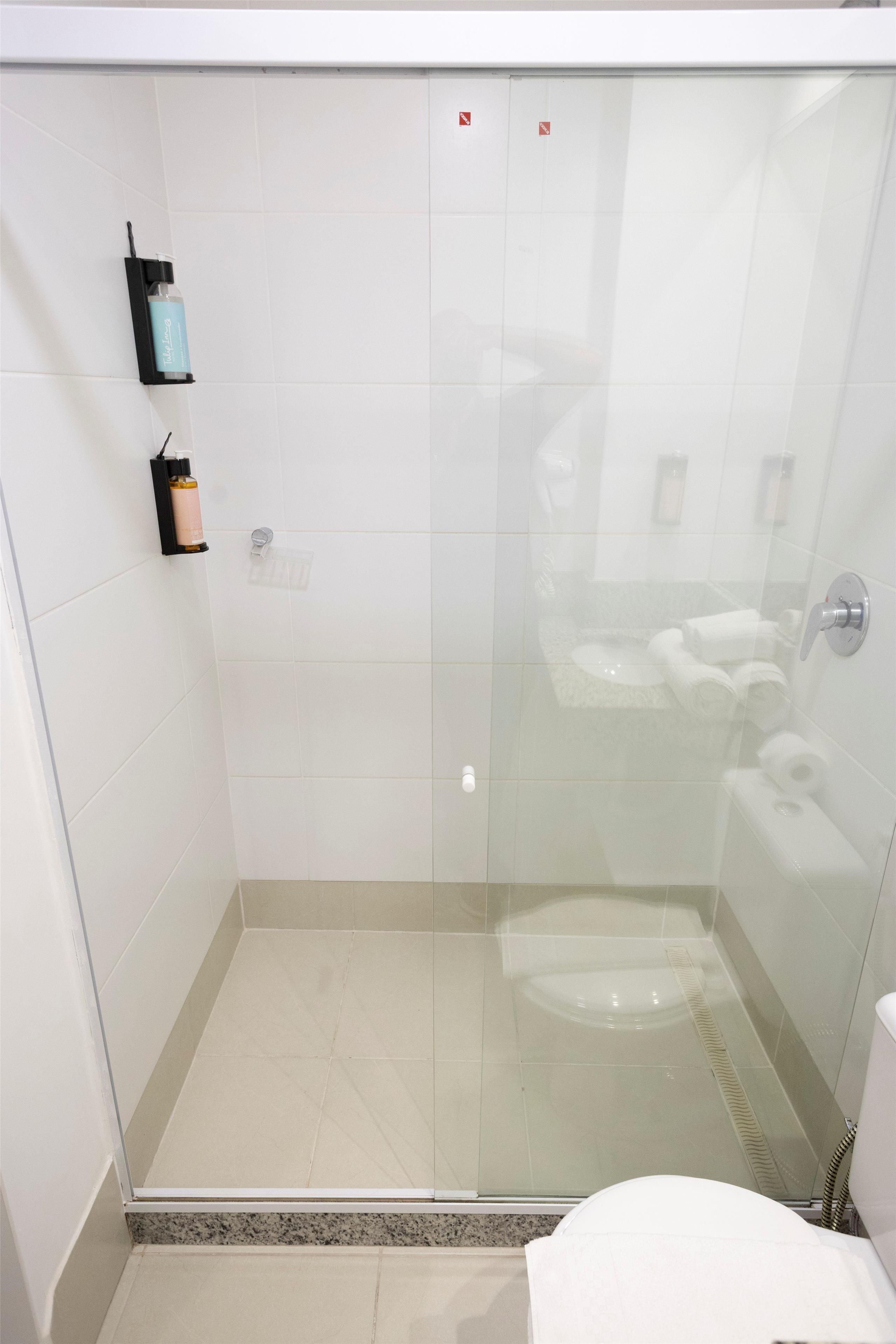 Box de chuveiro com paredes de vidro, vaso sanitário branco e porta-toalhas.