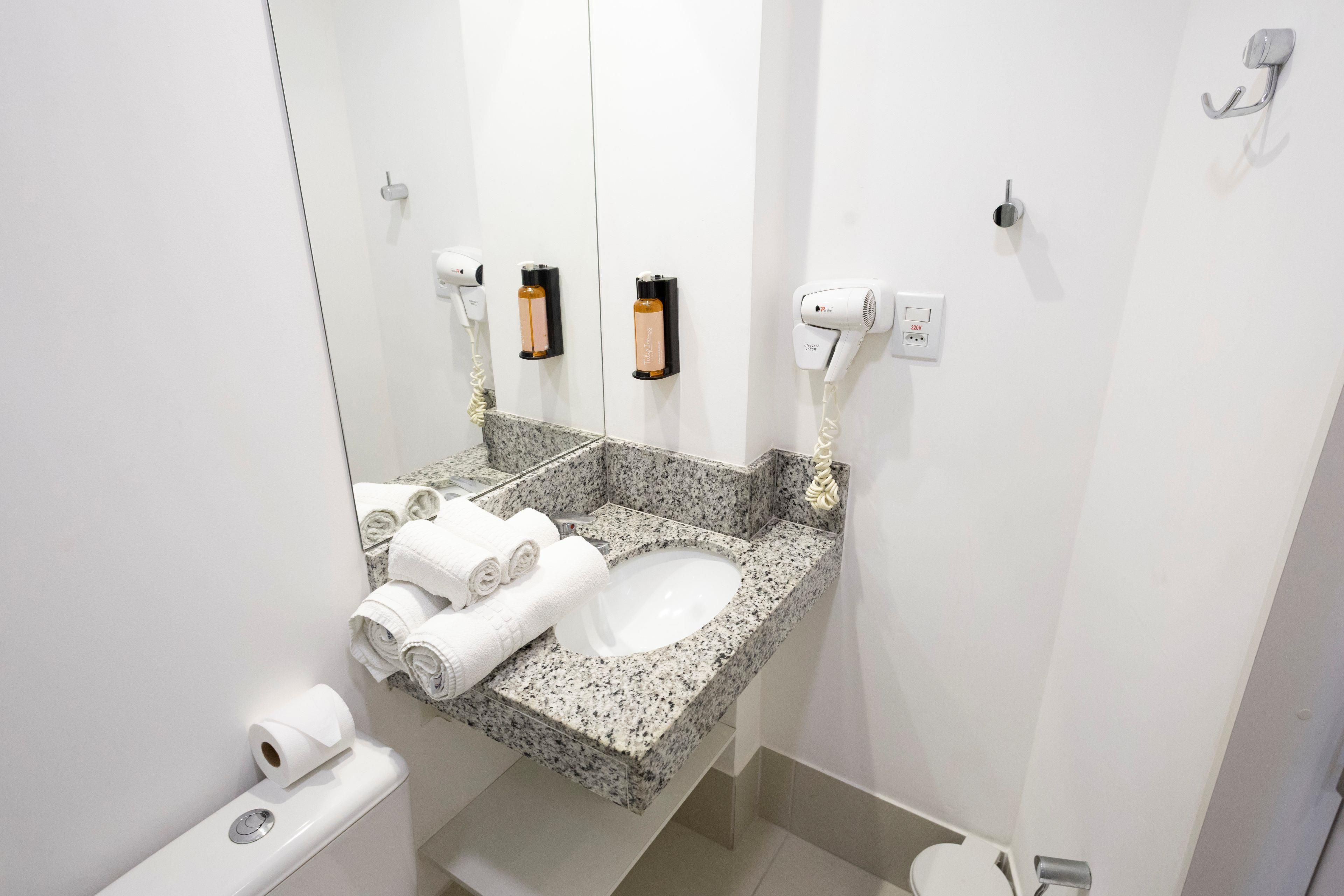 Ein Badezimmer mit Granitplatte, einem weißen Waschbecken, einem Spiegel, zwei Haartrocknern und einer Toilette.