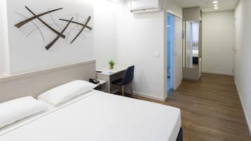 Habitación de hotel con cama, escritorio, silla, aire acondicionado y una planta pequeña.
