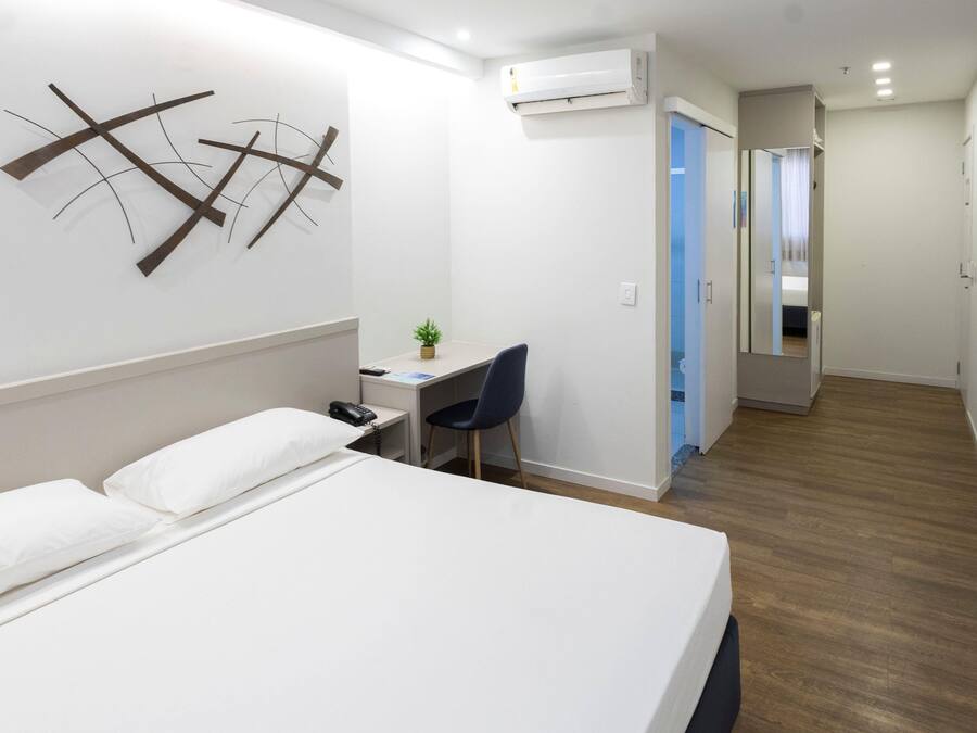Een hotelkamer met een bed, een bureau, een stoel, een airconditioner en een kleine plant.