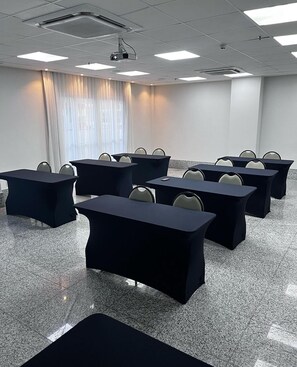 Un salón de conferencias con varias mesas y sillas, un proyector y un amplio ventanal con cortinas.