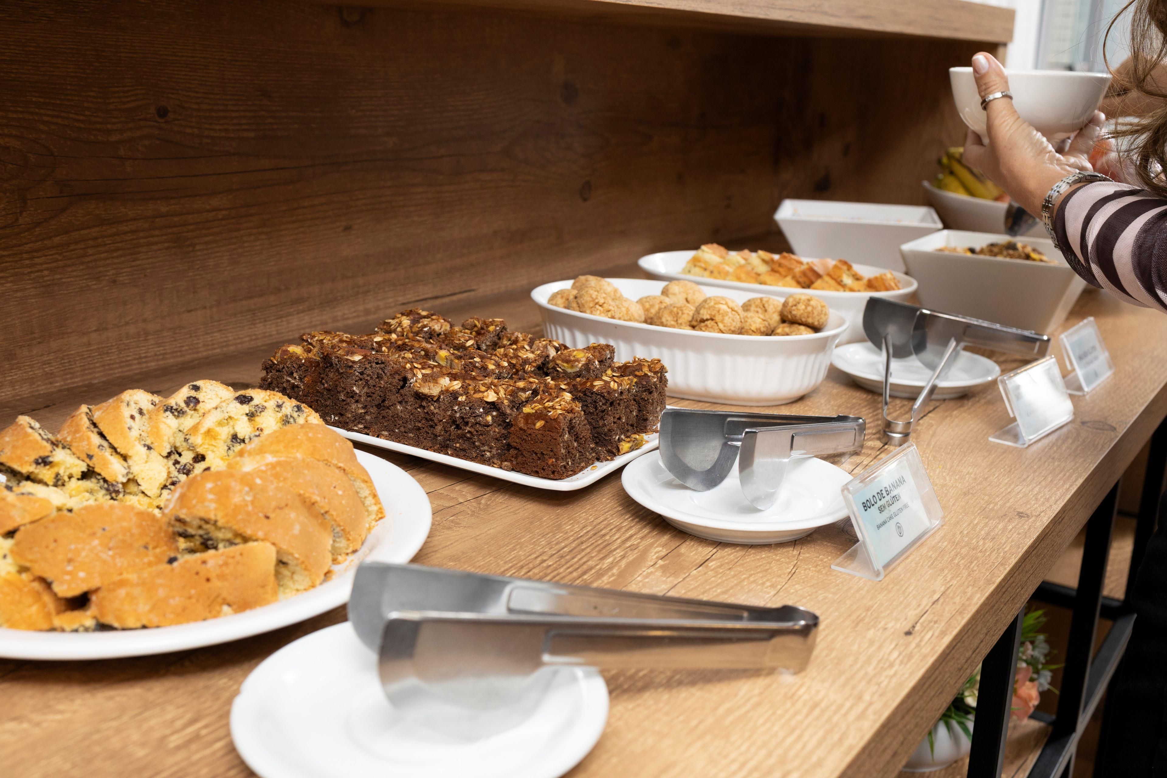 Una mesa de buffet con diversas opciones de repostería, incluyendo pasteles y galletas, y un letrero que indica una opción sin gluten.