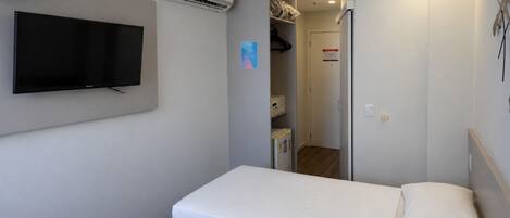 Habitación de hotel con dos camas, un televisor de pantalla plana, un equipo de aire acondicionado y una puerta que da a un pasillo.