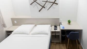 A hotel room with a bed, bedside table, desk, chair, and a wall-mounted telephone.