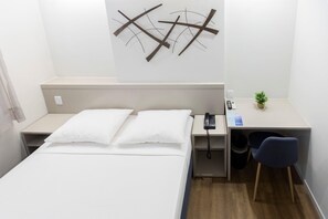 Hotellihuone, jossa on sänky, yöpöytä, työpöytä, tuoli ja seinälle asennettu puhelin.