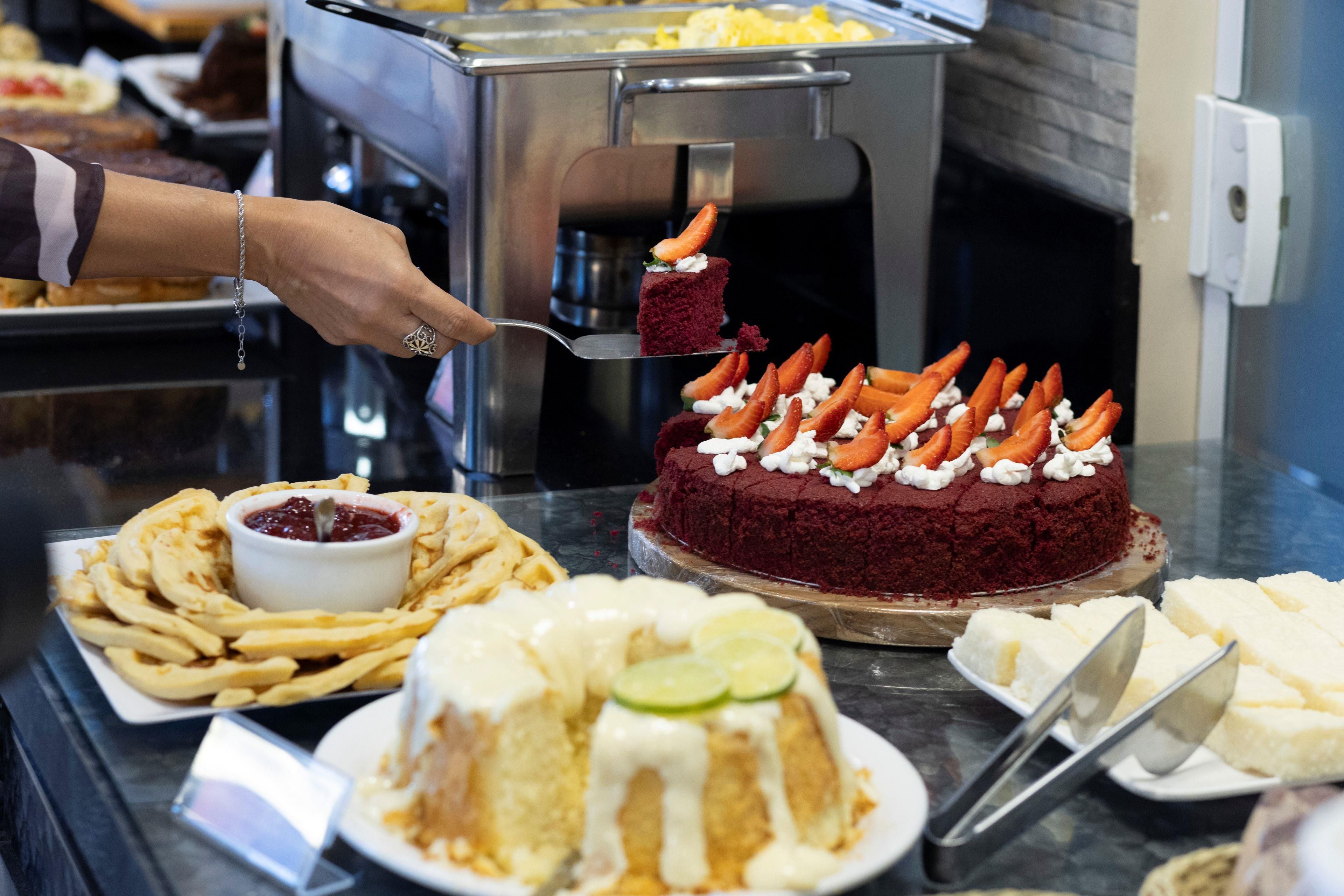 A buffet with various food items including a red velvet cake topped with strawberries and cream, a plate of French fries, and a dessert with whipped cream and lime slices.