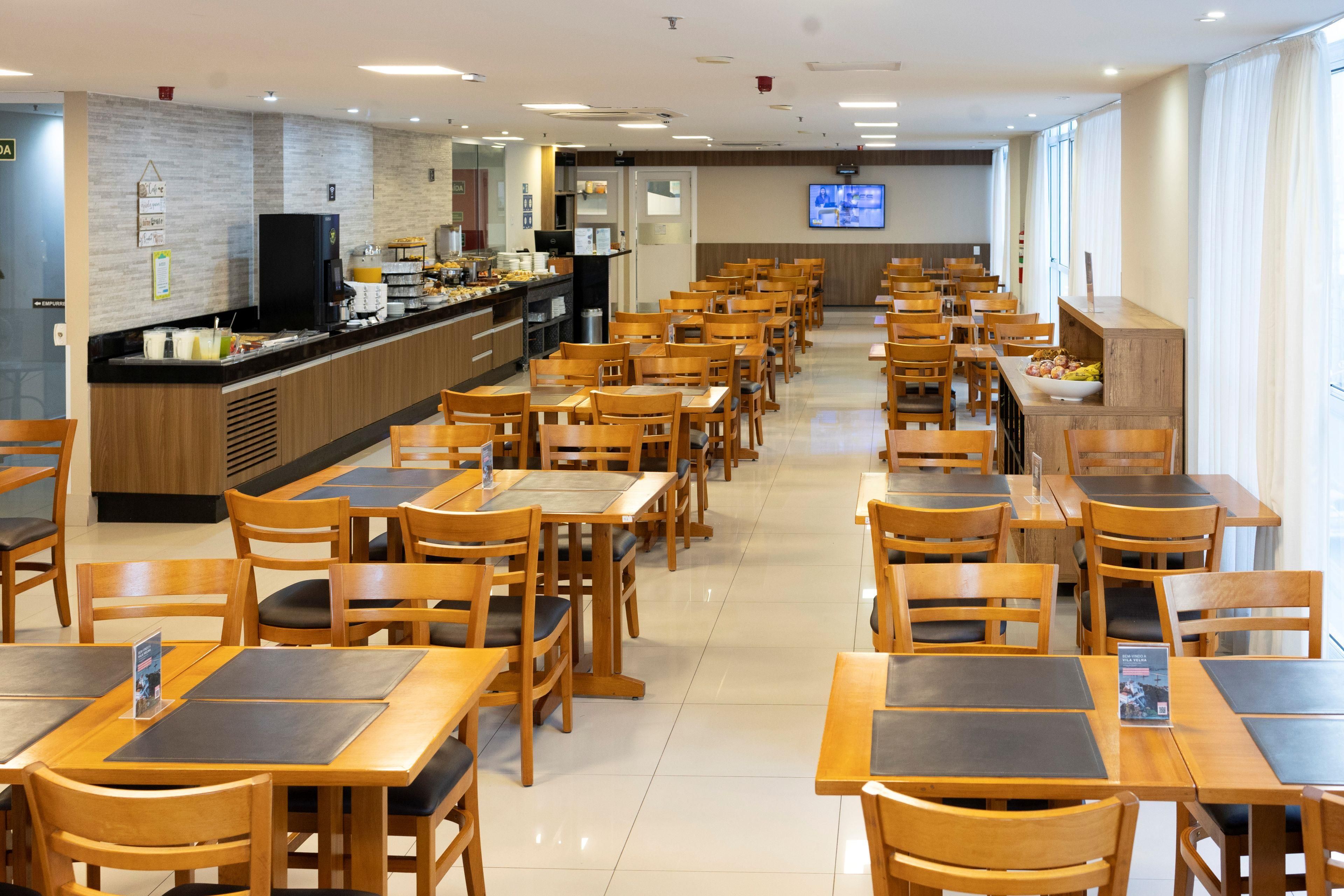 A spacious cafeteria with multiple tables and chairs, a buffet counter, and a television screen on the wall.