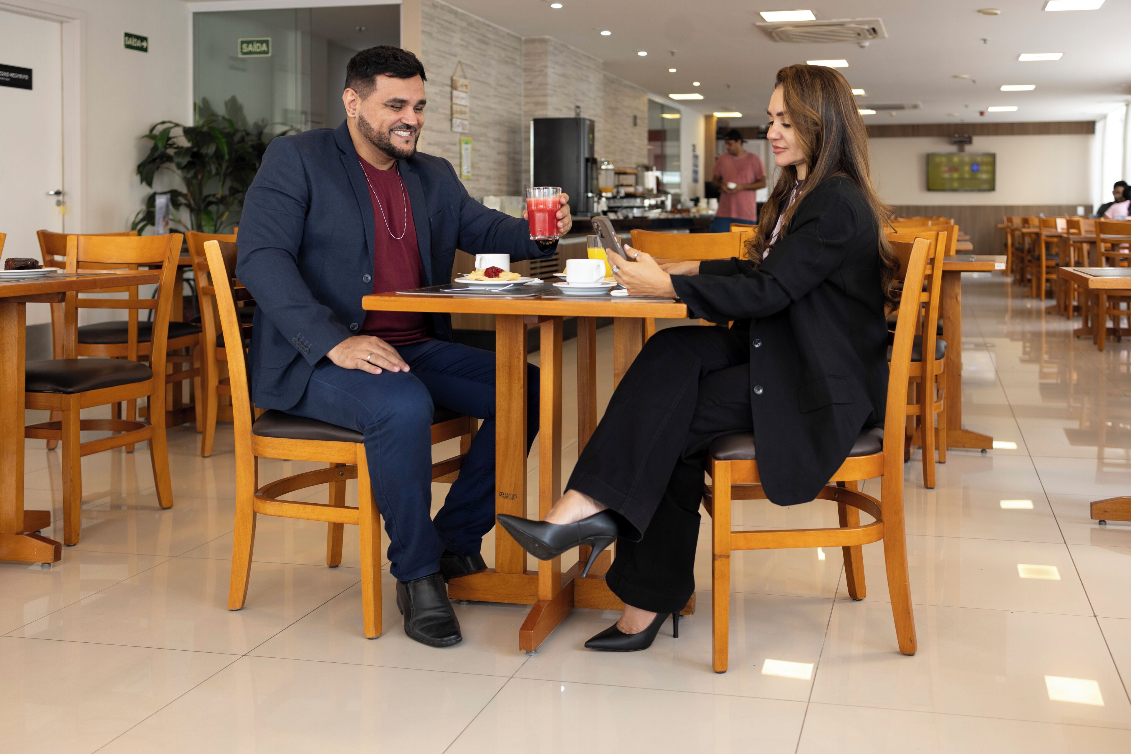 Un espace repas avec des chaises et des tables en bois, un homme et une femme assis à une table, devant une boisson et une tablette.