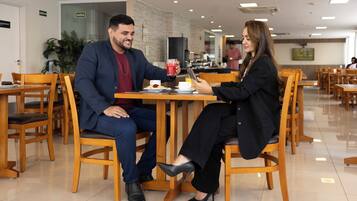 Un espace repas avec des chaises et des tables en bois, un homme et une femme assis à une table, devant une boisson et une tablette.