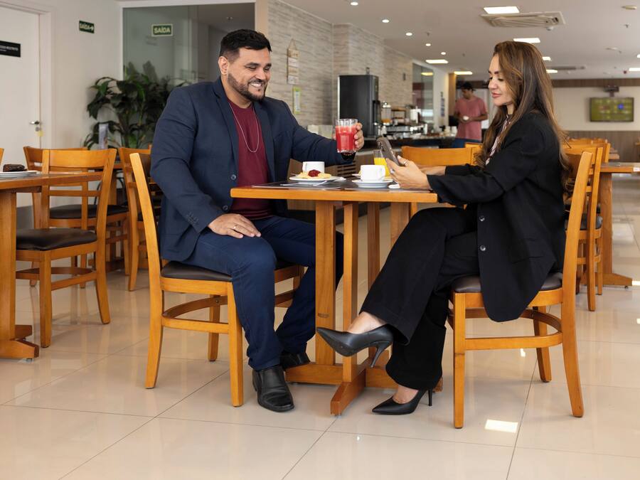 Un espace repas avec des chaises et des tables en bois, un homme et une femme assis à une table, devant une boisson et une tablette.