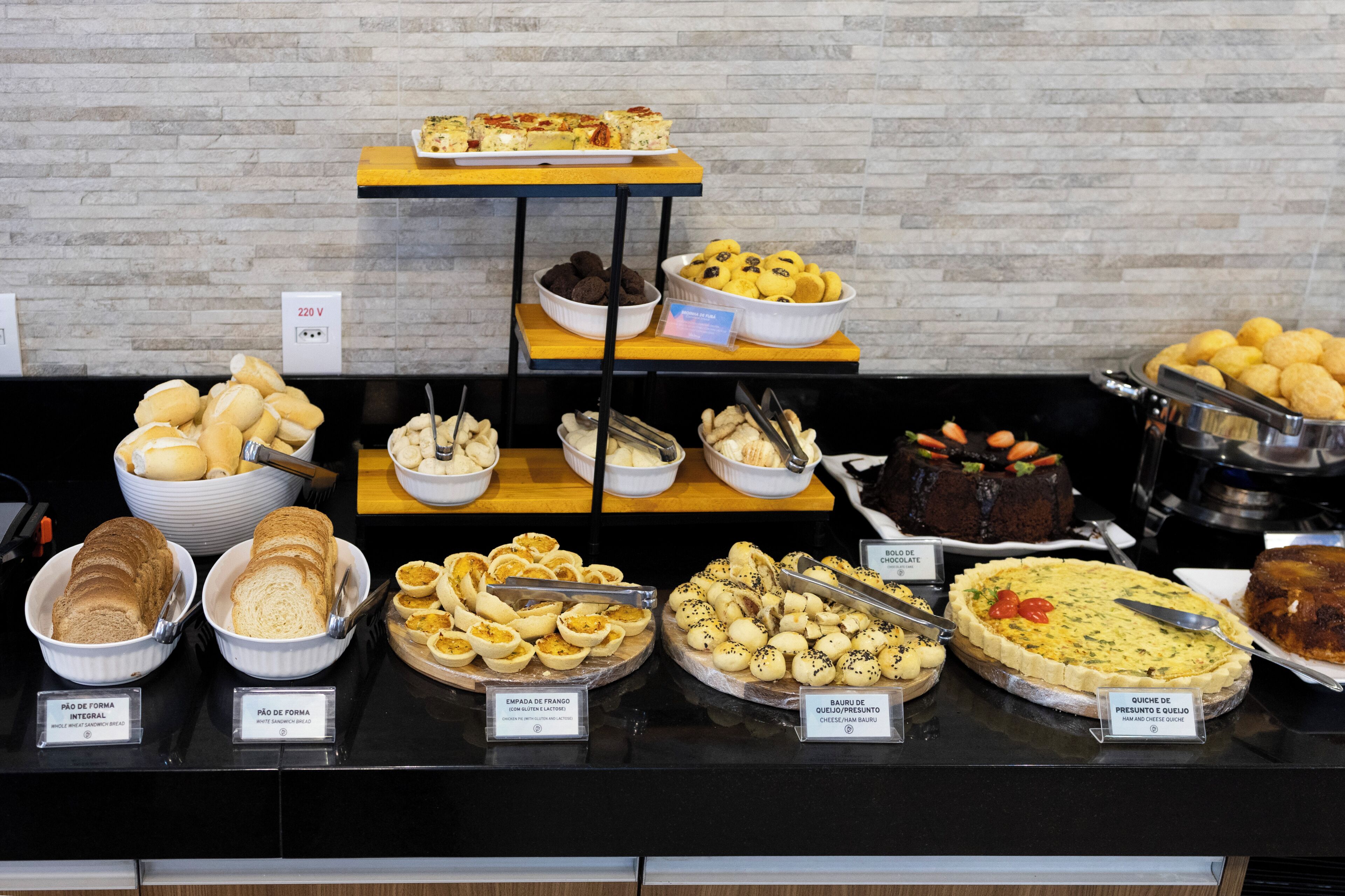 Buffet com diversos alimentos, incluindo pão, doces e uma quiche.