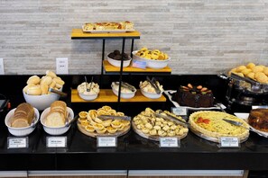 Un bufé con diversos alimentos, incluyendo pan, pasteles y una quiche.