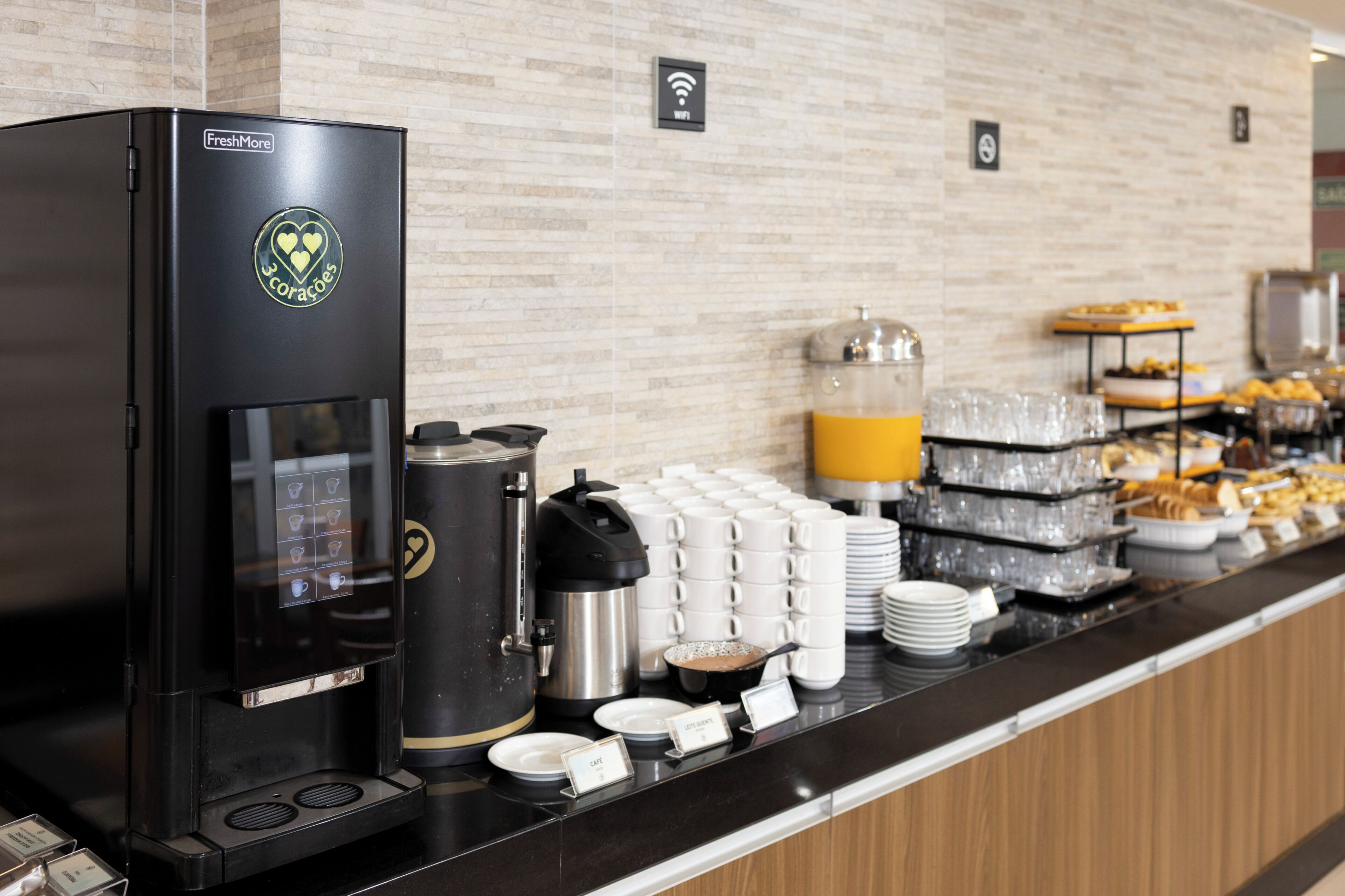 Una estación de café con una máquina de café de la marca, un dispensador de agua y diversas opciones para el desayuno, como pasteles y bebidas.