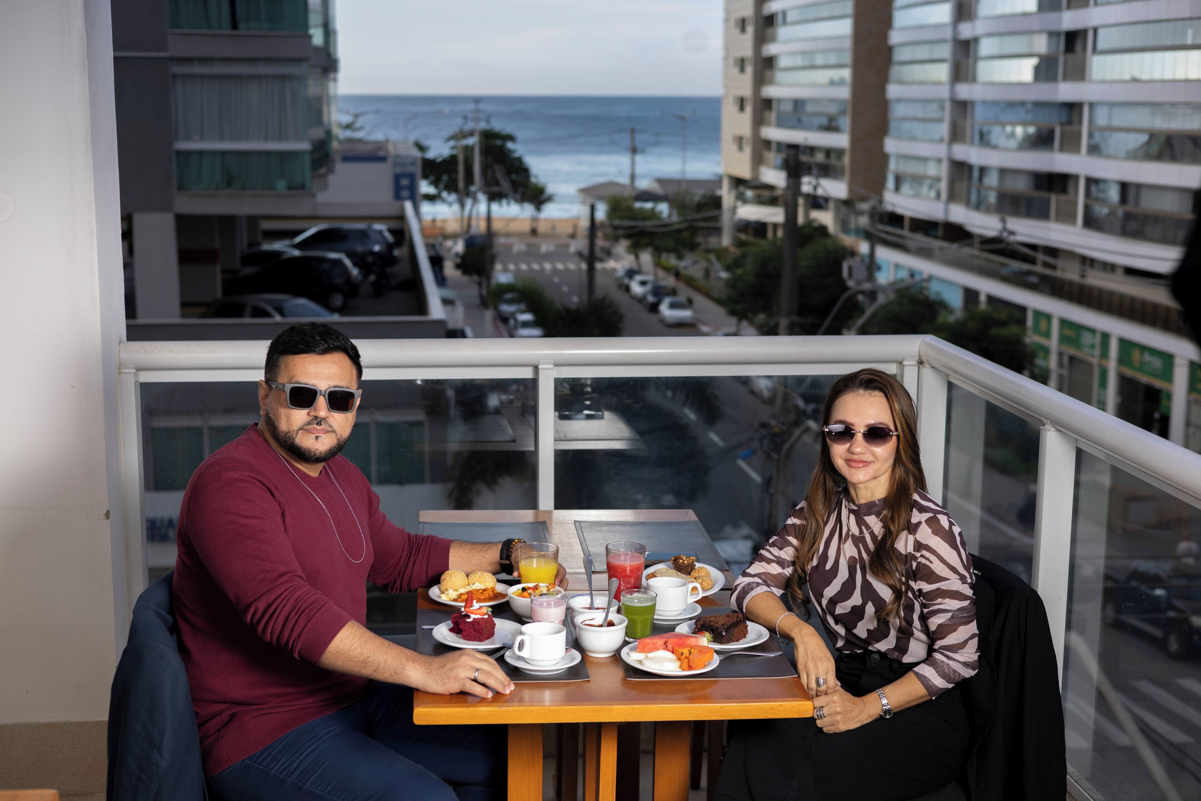 A balcony with a table set for two, overlooking a cityscape and the sea.