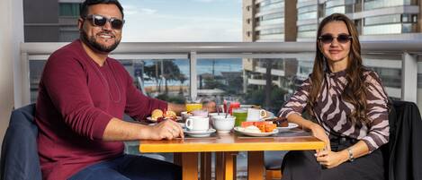 Una pareja cenando en una mesa con vistas a la ciudad, con diversos platos de desayuno y bebidas.