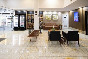 Un vestíbulo de hotel con mostrador de recepción, zona de estar y máquinas expendedoras.