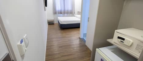 A hotel room with a bed, a small bedside table, a microwave, and a refrigerator.