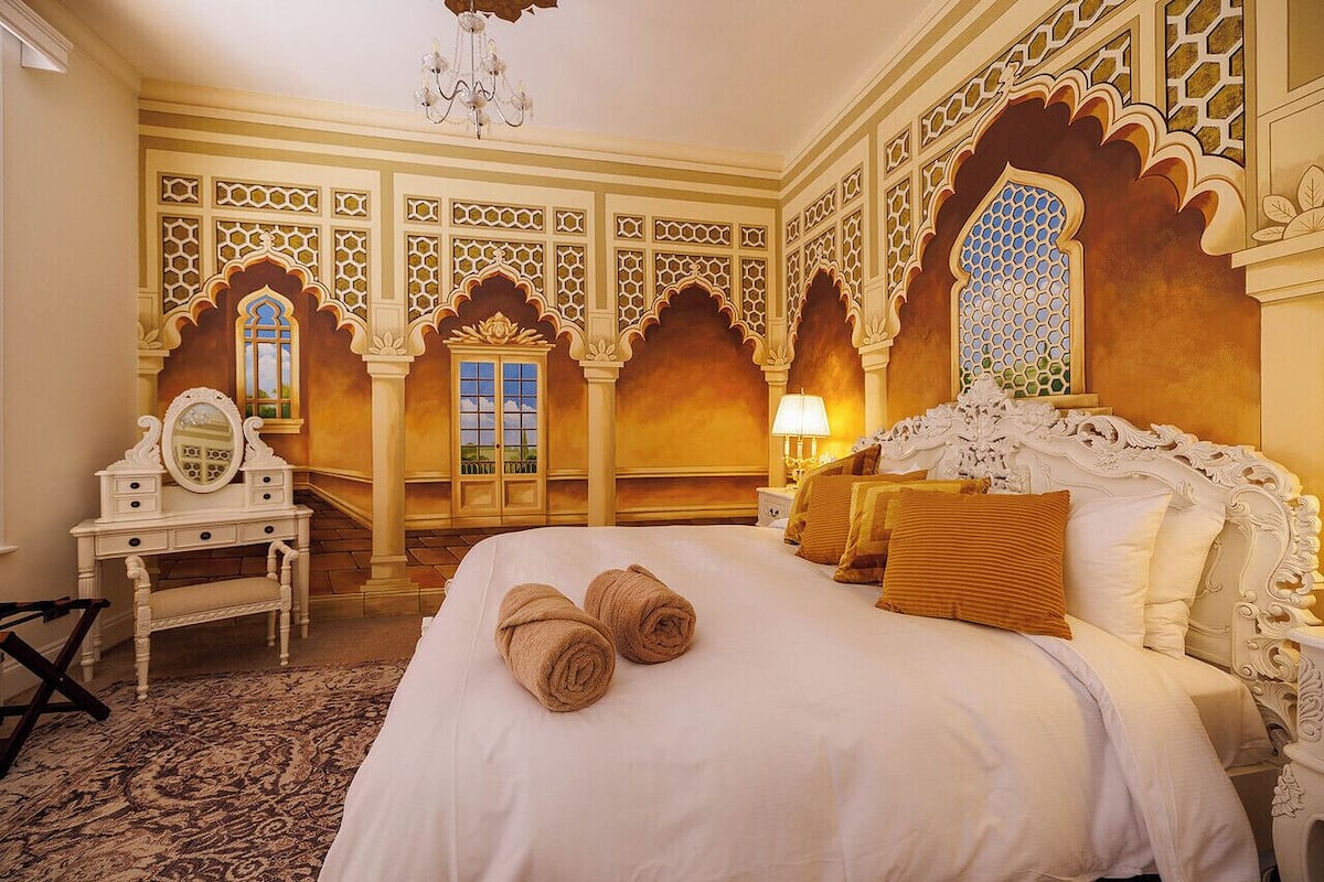 Une chambre d’hôtel avec un grand lit, des décorations murales élaborées et un lustre.