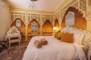 Una habitación de hotel con una cama grande, decoraciones ornamentales en la pared y un candelabro.