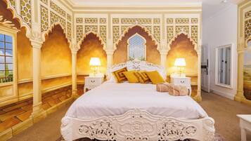 A large bed with ornate headboard, two bedside tables with lamps, and a patterned rug.