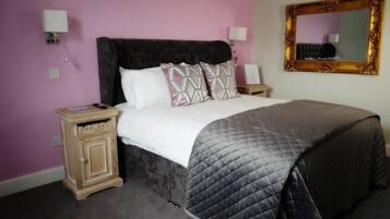 A bedroom with a bed, two nightstands, a mirror, and a wall-mounted light fixture.