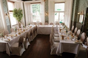 Un comedor formal con mesas largas dispuestas para una comida, rodeado de sillas con reposacabezas.