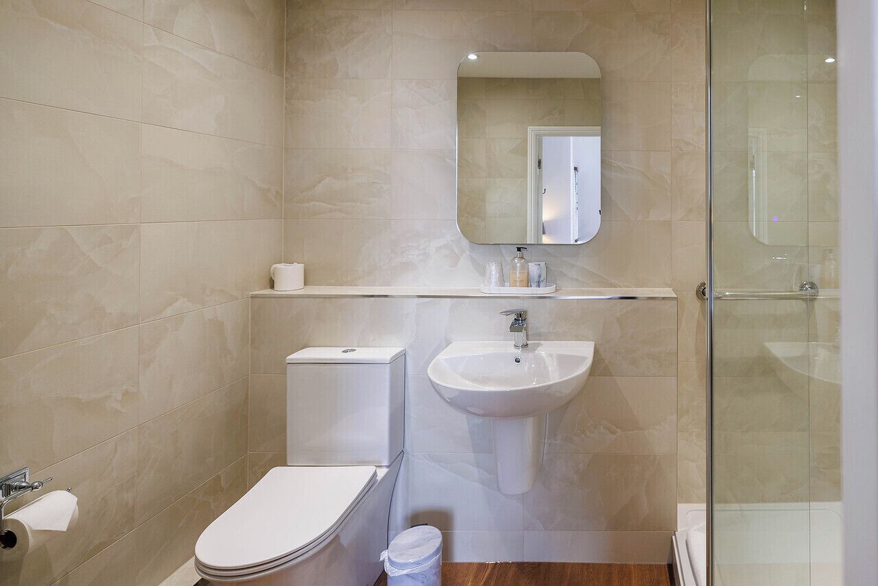 Un baño con inodoro, lavabo, espejo y ducha.