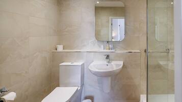 Un baño con inodoro, lavabo, espejo y ducha.