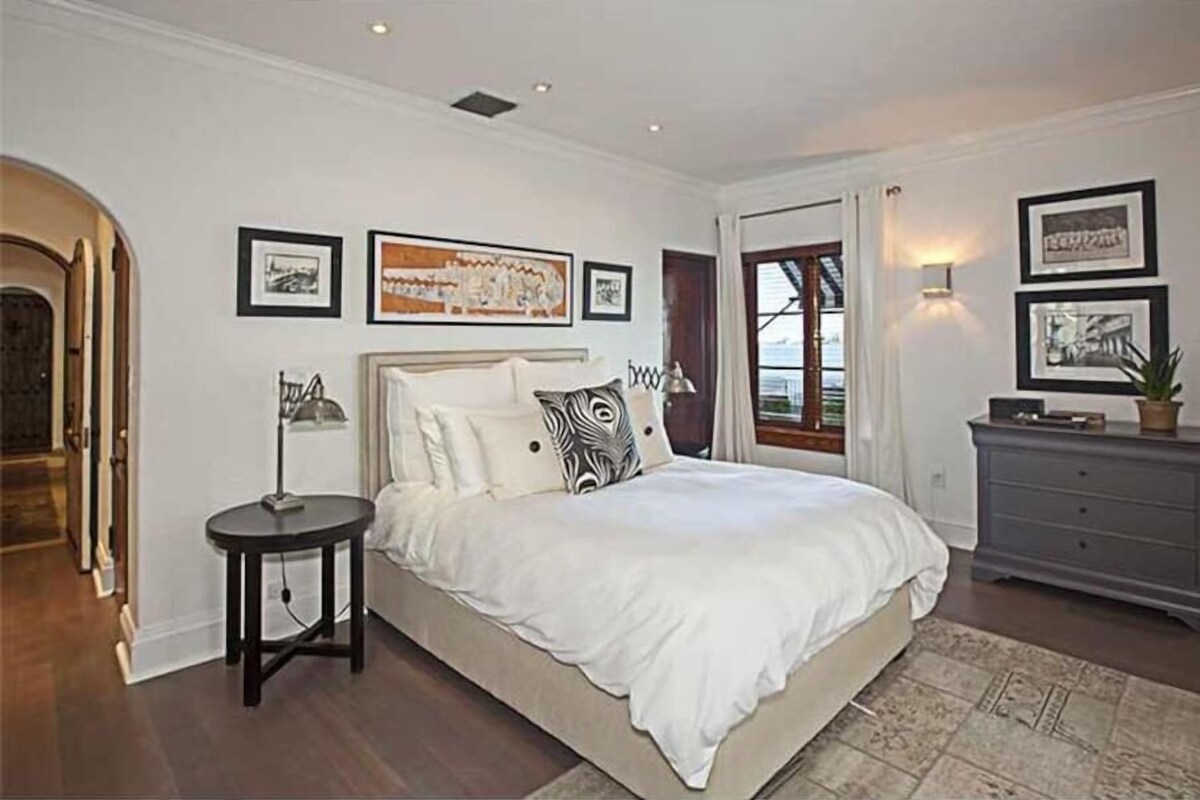 A bedroom with a large bed, a bedside table, a dresser, and framed artwork on the walls.