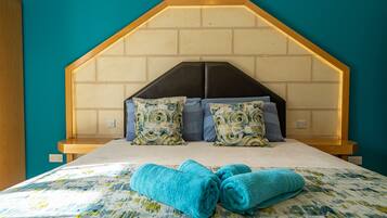 A bedroom with a wooden headboard, patterned pillows, and rolled towels on the bed.