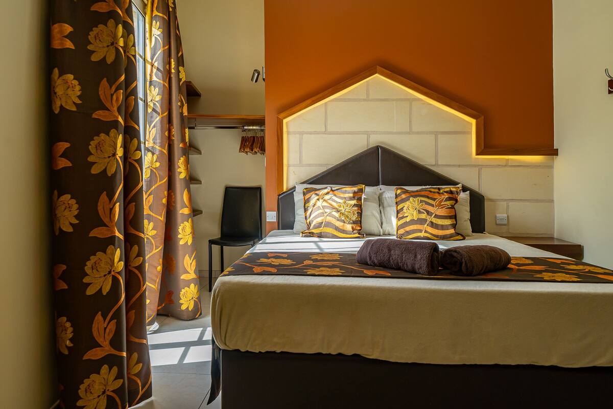 A neatly made bed with patterned pillows, a dark headboard, and a warm wall color.