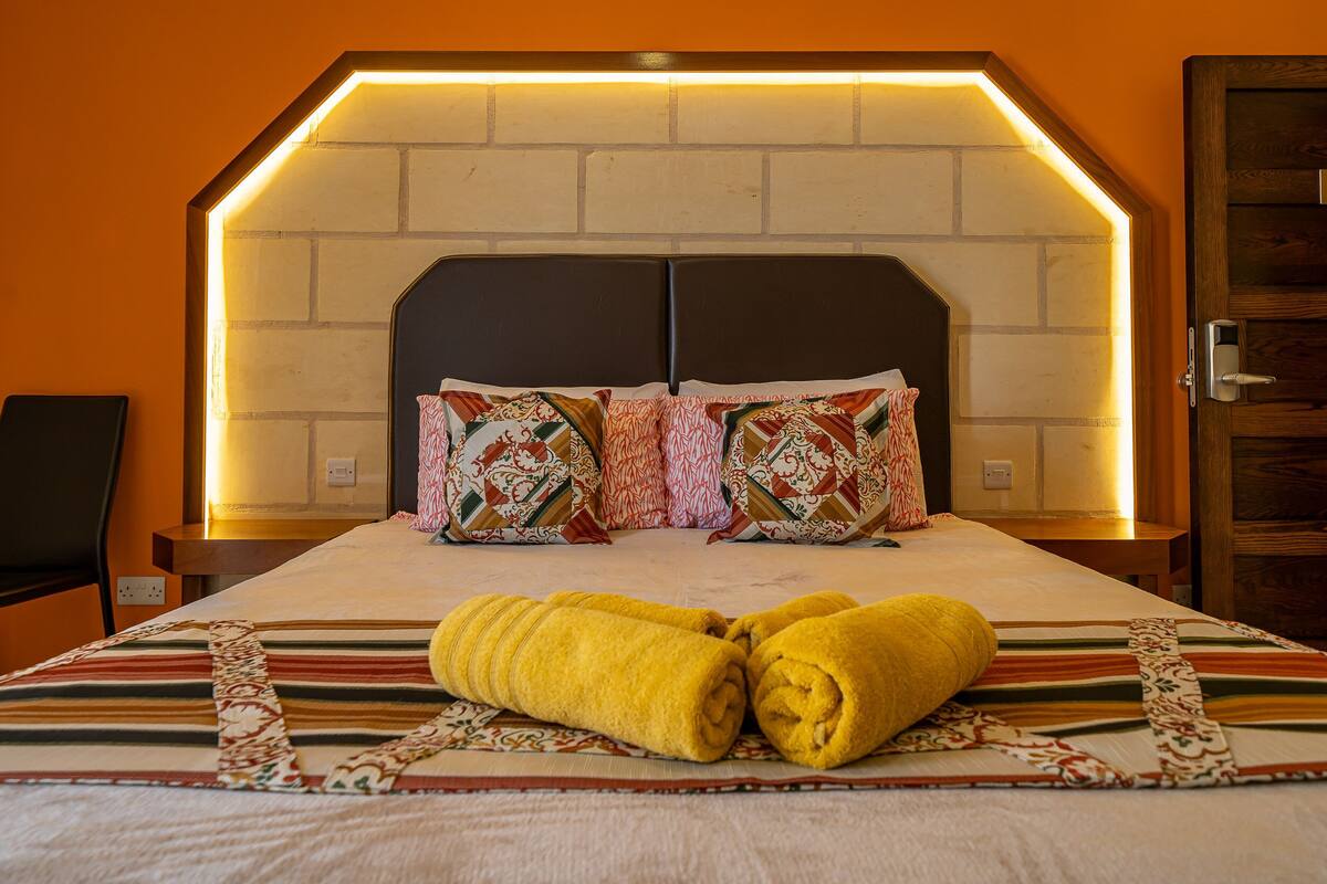 A hotel room with a brick-patterned headboard, two pillows, and two rolled towels on the bed.