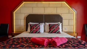 A hotel room with a brick-patterned headboard, two pillows with a red and black pattern, and a bed with a red and black floral bedspread.